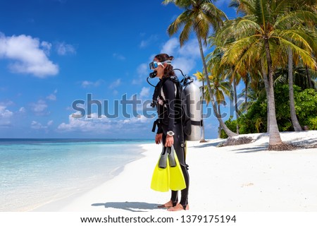 Female scuba diver in full equipment stands on a tropical beach ready to enter the water
