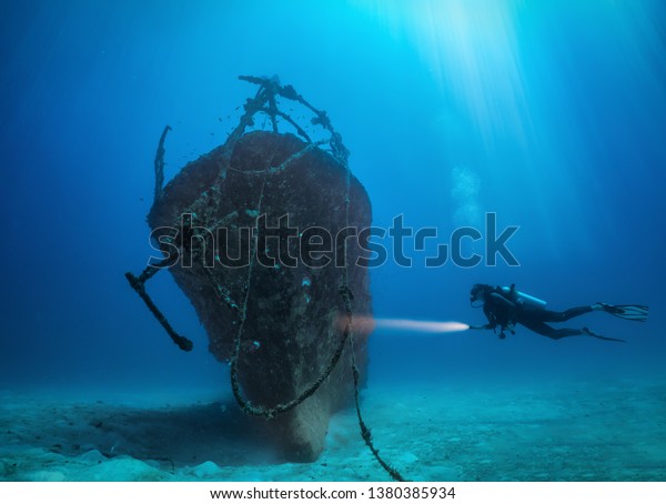Female scuba diver with a torch explores\
a sunken shipwreck at the Maldives\
islands