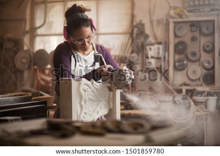 Female sculptor cutting a white marble piece with a power tool, craftswoman shaping a sculpture with an angle grinder, caucasian woman working inside an arts workshop, dust and debris flying away 