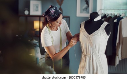 Female seamstress hand-stitching dress on dummy in sewing workshop, handmade clothes fabrication - Shutterstock ID 1830379985