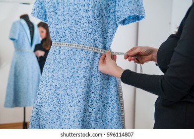 Female seamstress prepares dress to the fitting and takes measurements. Selective focus - Powered by Shutterstock