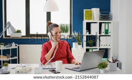 Female secretary using landline phone at company job, answering call from manager to plan financial strategy. Business employee working on research with office telephone conversation.