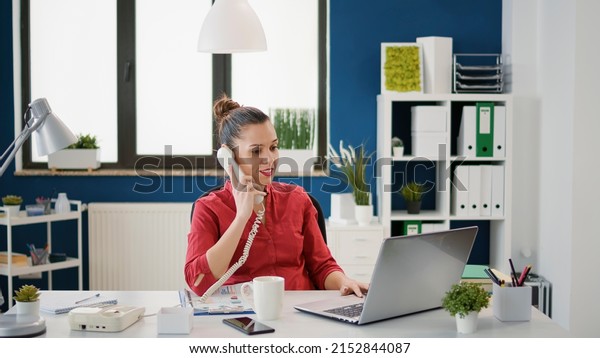 Female\
secretary using landline phone at company job, answering call from\
manager to plan financial strategy. Business employee working on\
research with office telephone\
conversation.