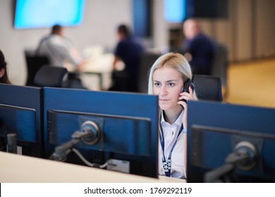 Female security guard operator talking on the phone while working at workstation with multiple displays Security guards working on multiple monitors