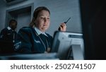 Female security officer or dispatch in uniform talks in walkie talkie, uses tablet computer and looks at screens in monitoring center during night shift. Surveillance, CCTV system and social safety.