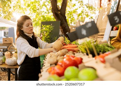 Female seller with an apron placing homegrown squash at farmers market stall booth. Young woman merchant examining locally grown fruits and vegetables on farm fair marketplace. - Powered by Shutterstock