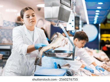 Vendedora en el departamento de pescado del supermercado pesa el bacalao atlántico en una balanza