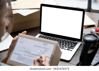 Female seller, internet shop small business owner holding ecommerce shipping box checking online store dropshipping order on mock up white blank laptop screen. E commerce post shipping delivery.