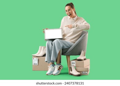 Vendedora con paquetes apuntando al portátil en sillón con fondo verde