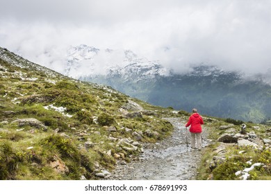 A Female Senior Hiker Wearing A Red Coat Hiking In The Paznaun Valley Near Galtur In Austria.