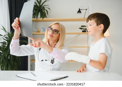 Female senior pediatrician showing x-ray of wrist and hand to little boy patient. Child at doctors office. - Powered by Shutterstock