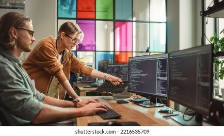 Female Senior Software Engineer Gives Advice To Male Junior Developer, Pointing At Desktop Computer Display With Code. Caucasian Woman Offers New Features, Helps Fixing Bugs In Modern SaaS Platform.