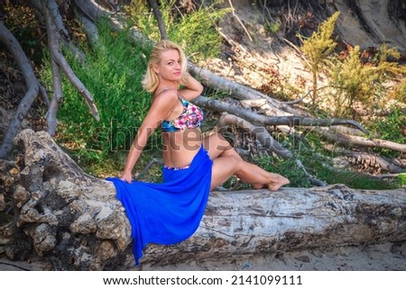 Female session in the wild seaside scenery. Beautiful woman sitting on a tree trunk by the Polish sea.