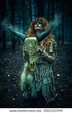 Female shaman in an ethnic dress doing a mysterious ritual with an animal skull. Portrait in a dark gloomy forest. Black magic concept, fantasy. Paganism. Halloween.