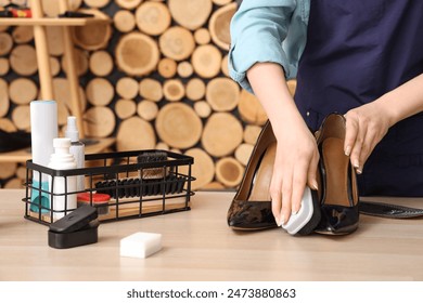 Female shoemaker polishing stylish high-heeled shoes at wooden table, closeup - Powered by Shutterstock