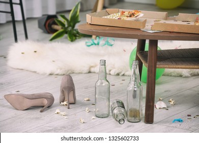 Female Shoes And Empty Bottles Near Table With Pizza Leftovers Indoors. After Party Chaos