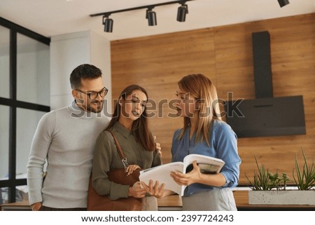 Female shop assistant helping young couple choose new kitchen appliance