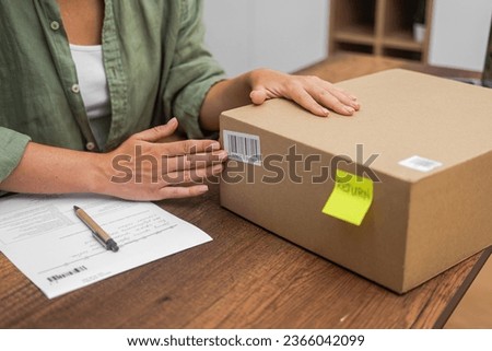 A female shopper attaches a barcode label to a cardboard box for an online shopping refund, streamlining the return process. 