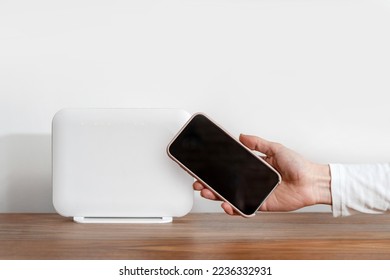 Female showing blank display on her phone with copy space for advertising internet provider services at home. Cropped shot of woman hand holding smartphone close to wi-fi router check connection speed