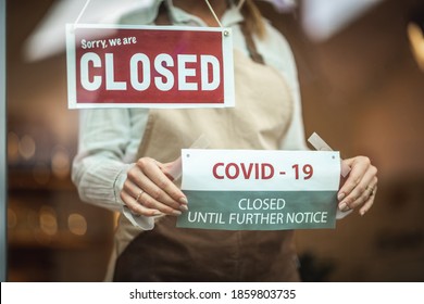 Female silhouette with a beige apron, standing behind the glass door with the sign ''closed'' and putting the covid19 notice