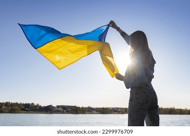 female silhouette holds a Ukrainian flag fluttering in the wind, beautifully illuminated by the sun. Ukrainians are against the war. Drawing attention to Ukraine. Stop the war - Powered by Shutterstock