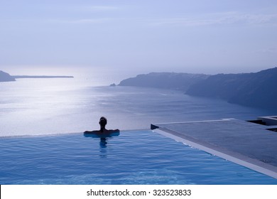 female silhouette in infinity pool on cliff looking out to sea, Santorini, Greece