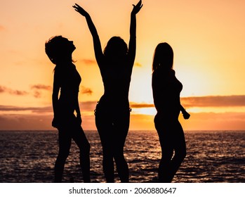 Female silhouettes in bikini on the sunset background. Golden hour party on a beach. Happy girls dancing