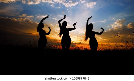Female silhouettes doing yoga in steppe, sunset background. Concept of asanas and meditation on nature.