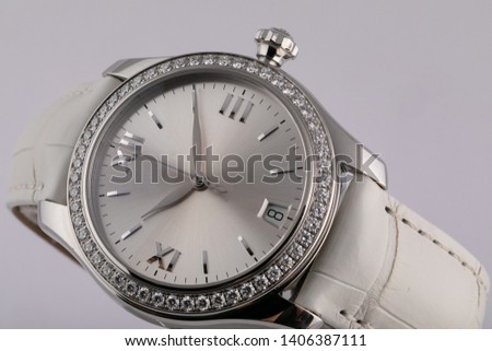 Female silver watch with a light grey dial, silver clockwise, chronograph, with a white leather strap, isolated on white background. 