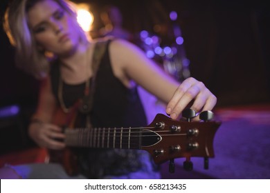 Female singer adjusting tuning peg of guitar in nightclub - Powered by Shutterstock