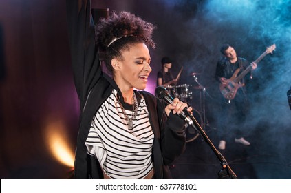 Female Singer With Microphone And Rock And Roll Band Performing Hard Rock Music On Stage  