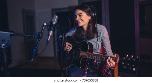 Female singer playing guitar and singing a song. Woman performing in a recording studio. Recording for her album. - Powered by Shutterstock