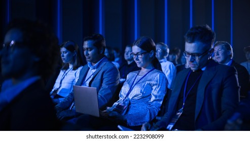 Female Sitting in a Dark Crowded Auditorium at a Tech Conference. Young Woman Using Laptop Computer. Specialist Watching Innovative Technology Presentation About New Software and High Tech Products. - Powered by Shutterstock