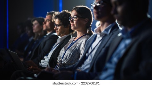 Female Sitting in a Dark Crowded Auditorium at a Tech Conference. Young Woman Using Laptop Computer. Specialist Watching Innovative Technology Presentation About New Software and High Tech Products. - Powered by Shutterstock