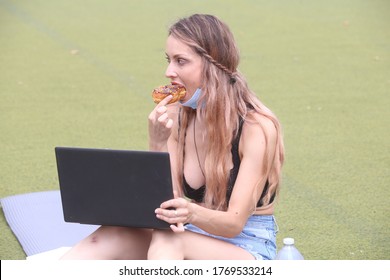 Female Sitting Down Outside Eating A Doughnut While Working On A Computer