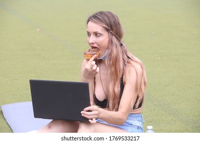 Female Sitting Down Outside Eating A Doughnut While Working On A Computer