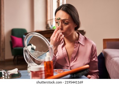 Female Is Sitting In Front Of Mirror In Living Room And Using Jade Roller On Her Face