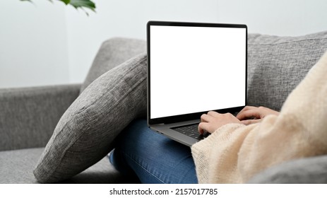 Female Sitting On Comfy Sofa And Using Laptop Computer Browsing On The Internet In Her Living Room. Laptop Computer White Screen Mockup.