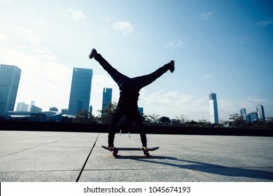 Female Skateboarder Doing A Handstand On Skateboard In City