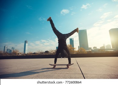 Female Skateboarder Doing A Handstand On Skateboard In City