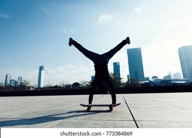 Female Skateboarder Doing A Handstand On Skateboard In City