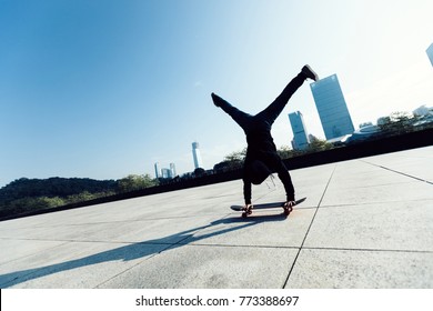 Female Skateboarder Doing A Handstand On Skateboard In City