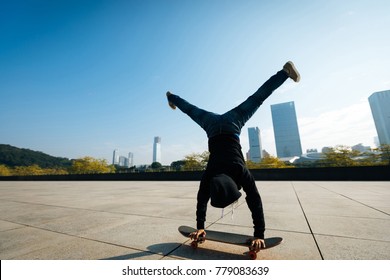 Female Skateboarder Doing A Handstand On Skateboard In City