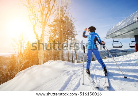 Female skier on the top of ski slope with ski-lift and mountains on the background. Winter sports concept. Girl is looking at beautiful mountain landscape on sunny day. Bukovel, Ukraine