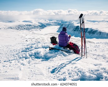 Female skier resting at a norwegian mountain summit having her moment at easter admiring a panoramic view towards a frozen lake and with a low cloud base with snow showers in the horizons