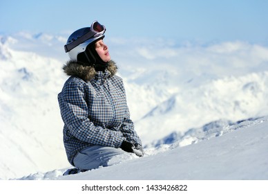 Female Skier Sitting In Snow Enjoying Sun At Ski Resort In Austrian Alps