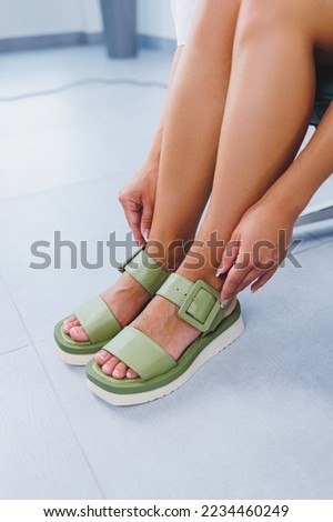 Female slender legs in green summer sandals. Women's leather shoes
