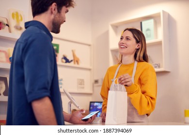 Female Small Business Owner Accepting Contactless Payment In Shop From Customer Using Mobile Phone