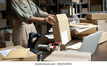 Female small business owner, entrepreneur, shipment delivery dropshipping service worker packing ecommerce order package in shipping cardboard box standing at table in warehouse. Close up view