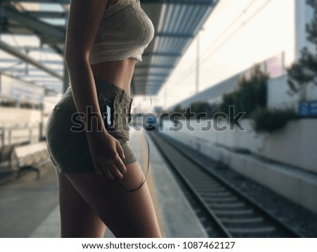 Female with smartphone and headphones stands on the platform waiting for the train